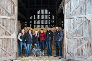 The Haanover View Farm Family and dog standing in front of an open barn door with straw bales in the background.
